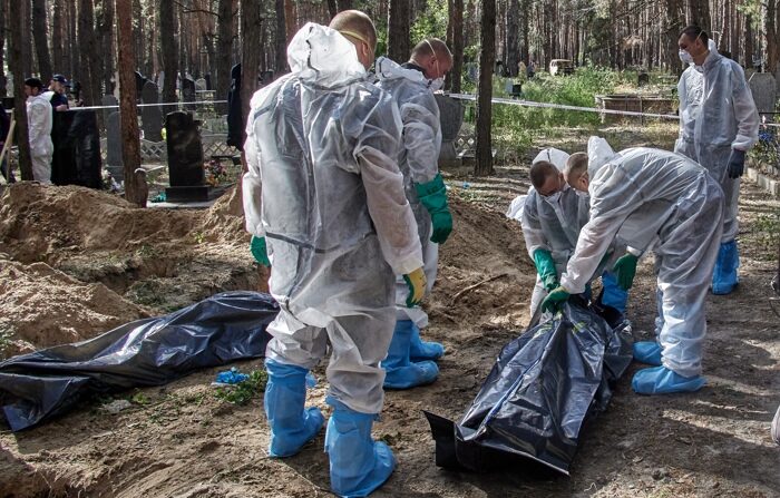 Trabalhadores ucranianos revisam corpos desenterrados de sepulturas em Izyum, na região de Kharkov, no nordeste da Ucrânia, em 19 de setembro de 2022 (EFE/EPA/SERGEY KOZLOV)