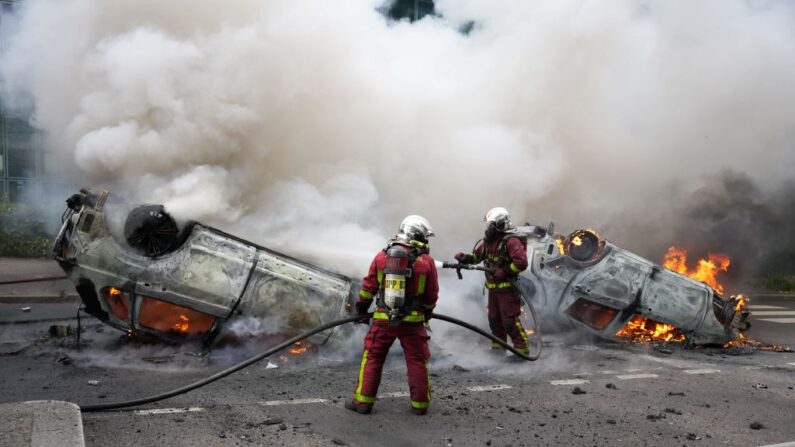 Bombeiros extinguem carros em chamas em uma rua quando confrontos eclodiram no final de uma marcha em homenagem a um motorista adolescente morto a tiros por um policial, no subúrbio parisiense de Nanterre em 29 de junho de 2023 (Foto de ZAKARIA ABDELKAFI/AFP via Getty Images)