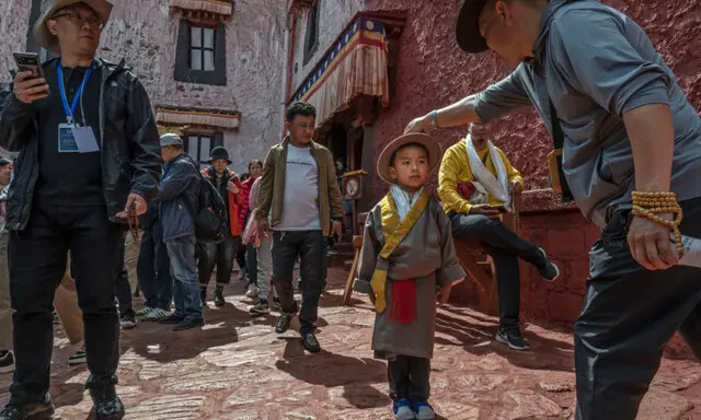 Um homem budista tibetano ajusta o chapéu de um menino em roupas tradicionais enquanto visita o Palácio de Potala, um Patrimônio Mundial da UNESCO, durante uma visita organizada pelo governo em Lhasa, Tibete, China, em 16 de junho de 2023. (Kevin Frayer/Getty Images )