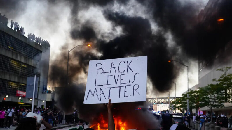 Um homem segura uma placa do Black Lives Matter enquanto um carro da polícia queima na frente dele durante um protesto pela morte de George Floyd, fora do CNN Center em Atlanta, em 29 de maio de 2020 (Elijah Nouvelage/Getty Images)