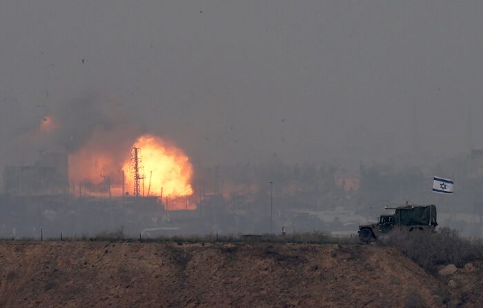 Um veículo militar israelense avança ao longo da fronteira com a Faixa de Gaza, no sul de Israel, enquanto uma explosão ocorre ao fundo durante um ataque aéreo na terça-feira (EFE/ Atef Safadi).