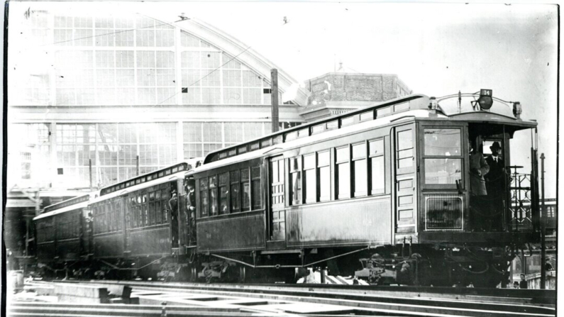 Um teste de 1900 de um motor de trem de controle de múltiplas unidades na estação Sullivan Square em Boston, Massachusetts. Acredita-se que a figura da extrema direita seja Frank J. Sprague, o inventor da unidade. (Domínio público)
