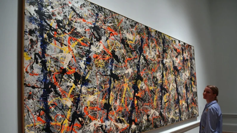 Um membro da equipe posa ao lado de uma pintura do artista norte-americano Jackson Pollock intitulada “Blue Poles” na Royal Academy of Arts de Londres em 20 de setembro de 2016 (Carl Court/Getty Images)