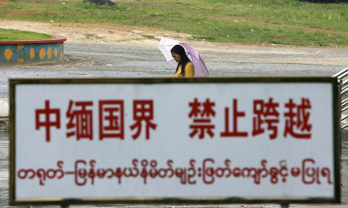 Uma mulher birmanesa caminha atrás de uma placa de alerta ao longo da linha de fronteira na cidade fronteiriça de Wanding, na China-Birmânia, na província de Yunnan, no sudoeste da China, em 27 de setembro de 2007. (STR/AFP via Getty Images)
