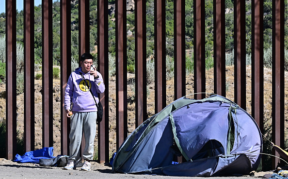 Um imigrante chinês usa seu celular ao lado do muro da fronteira entre os EUA e o México depois que grupos de imigrantes entraram nos EUA vindos do México em Jacumba Hot Springs, Califórnia, em 5 de junho de 2024. Os Estados Unidos fecharão temporariamente sua fronteira com o México para requerentes de asilo a partir de hoje, 5 de junho, enquanto o presidente Joe Biden tenta neutralizar sua fraqueza política em relação à Imigração antes da dispita eleitoral de novembro contra Donald Trump. Biden assinou uma ordem executiva para "ganhar o controle" da fronteira sul com o México, depois que um número recorde de travessias ilegais da fronteira gerou preocupações entre eleitores. (FREDERIC J. BROWN/AFP via Getty Images)