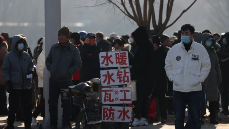 Trabalhadores migrantes em pé perto de placas anunciando suas habilidades enquanto esperam em uma rua para serem contratados em Shenyang, província de Liaoning, China, em 6 de fevereiro de 2023. (STR/AFP via Getty Images)