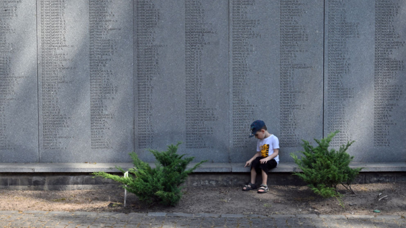 Uma criança senta-se em um memorial durante uma cerimônia que marca o Dia da Lembrança das Vítimas da Repressão Política na Reserva Nacional Histórica e Memorial "Sepulturas de Bykivnia" para homenagear as cerca de 100.000 pessoas baleadas pelo regime de Stalin e enterradas na vala comum na floresta de Bykivnia, nos arredores de Kiev, em 19 de maio de 2024 (Foto de SERGEI SUPINSKY/AFP via Getty Images)