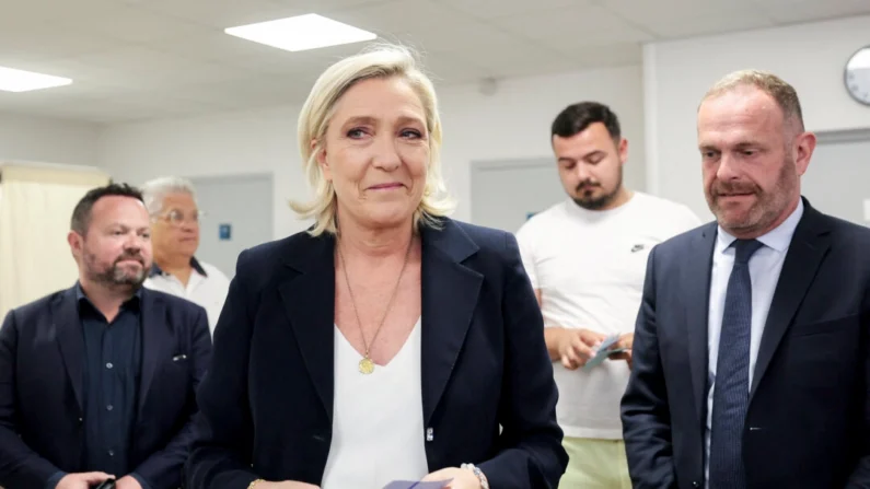 Marine Le Pen (centro), líder do partido francês Reagrupamento Nacional, segura cédulas de votação ao lado do prefeito de Henin-Beaumont, Steeve Briois (direita), antes de votar no primeiro turno das eleições parlamentares em Henin-Beaumont, norte da França, em 30 de junho de 2024. (Francois Lo Presti/AFP via Getty Images)
