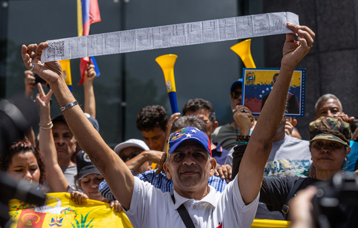 Um homem mostra uma cédula do Conselho Nacional Eleitoral da Venezuela (CNE) com os resultados de uma mesa de votação durante uma manifestação em apoio ao candidato presidencial venezuelano Edmundo Gonzalez Urrutia, na terça-feira, 30 de julho de 2024, em Caracas, Venezuela (EFE/ Henry Chirinos)