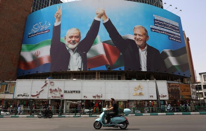 Iranianos passam por um cartaz que mostra o líde iraniano Massed Pezeshkian (dir.) e o falecido líder político do Hamas, Ismail Haniyeh, na Praça Valiasr, em Teerã (EFE/EPA/ABEDIN TAHERKENAREH)