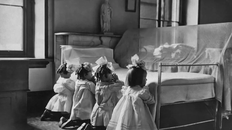 Quatro meninas orando ao lado de uma cama em um hospital para enjeitados, por volta de 1920 (Paul Thompson/FPG/Archive Photos/Getty Images)
