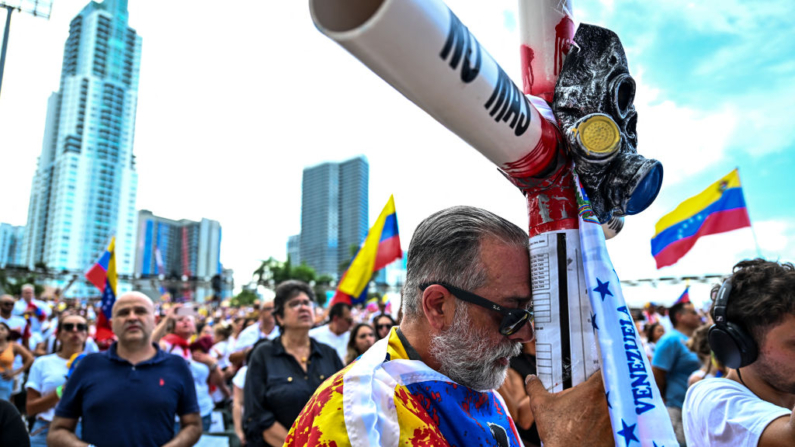 Gaston Gonzalez reza com uma cruz onde se lê "Chega de Comunismo" enquanto participa do protesto "Protesto pela Verdade", convocado pela oposição venezuelana para exigir que o governo venezuelano reconheça a vitória de Edmundo Gonzalez Urrutia nas eleições presidenciais, em Miami, Flórida, em 17 de agosto de 2024 (Foto de CHANDAN KHANNA/AFP via Getty Images)