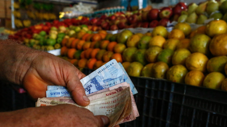 Um cliente conta dinheiro em uma banca de frutas e legumes em um mercado em Salvador, Bahia, Brasil, em 26 de agosto de 2022 (Foto de RAFAEL MARTINS/AFP via Getty Images)