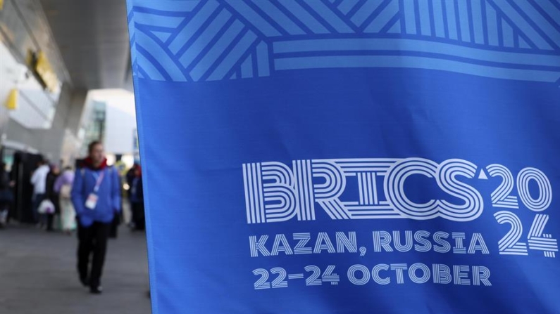 Kazan (Federação Russa), 20/10/2024 - Pessoas em pé atrás da faixa do BRICS 2024 em sua chegada ao aeroporto de Kazan, Rússia, em 20 de outubro de 2024. A Rússia receberá líderes de 24 países e delegações de 32 países na próxima cúpula do BRICS em Kazan, disse o assessor presidencial russo Yuri Ushakov. Prevista para ser o maior evento de política externa da história da Rússia, a cúpula do BRICS será realizada de 22 a 24 de outubro (EFE/EPA/MAXIM SHIPENKOV)