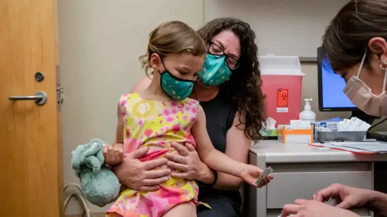 Uma menina de 3 anos senta no colo da mãe em uma foto de arquivo durante uma vacinação (David Ryder/Getty Images)