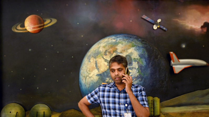 Um membro da Organização de Pesquisa Espacial Indiana (ISRO) fica em frente a um mural que retrata a exploração espacial enquanto atende a uma chamada telefônica durante um workshop sobre defesa planetária na sede da ISRO em Bengaluru, em 3 de julho de 2024 (Foto de IDREES MOHAMMED/AFP via Getty Images)