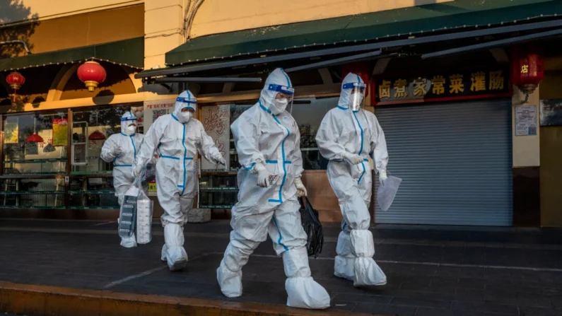 Trabalhadores de controle da pandemia passam por uma loja fechada perto de uma comunidade com moradores sob monitoramento de saúde para COVID-19 em Pequim, em 4 de dezembro de 2022. Imagens de Kevin Frayer/Getty
