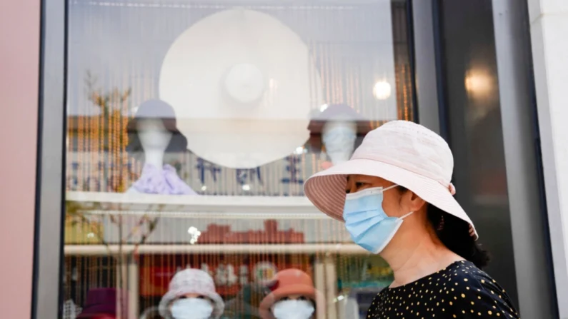 Uma mulher usando máscara passa por cabeças de manequim usando máscaras em uma loja de chapéus em Pequim, em 9 de setembro de 2022. (Ng Han)
