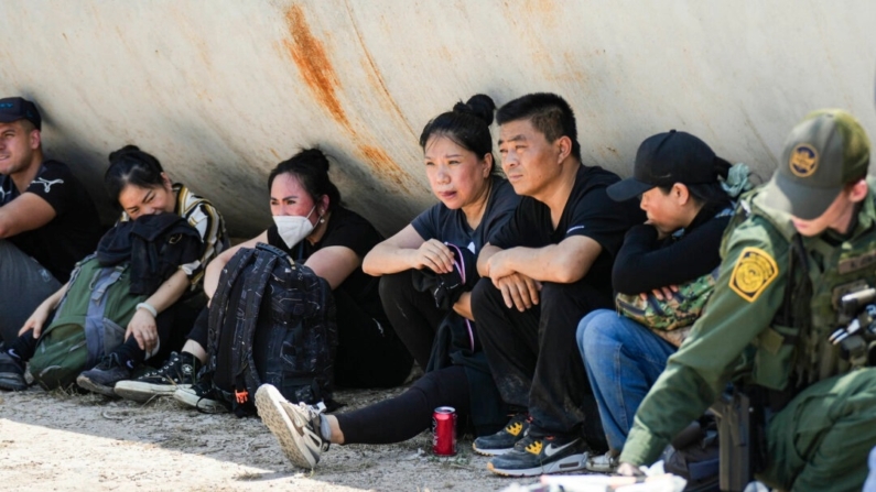 Imigrantes ilegais chineses esperam enquanto agentes da Patrulha de Fronteira prestam atendimento médico a uma mulher de um grande grupo de imigrantes ilegais perto de Eagle Pass, Texas, em 20 de maio de 2022. (Charlotte Cuthbertson/Epoch Times)