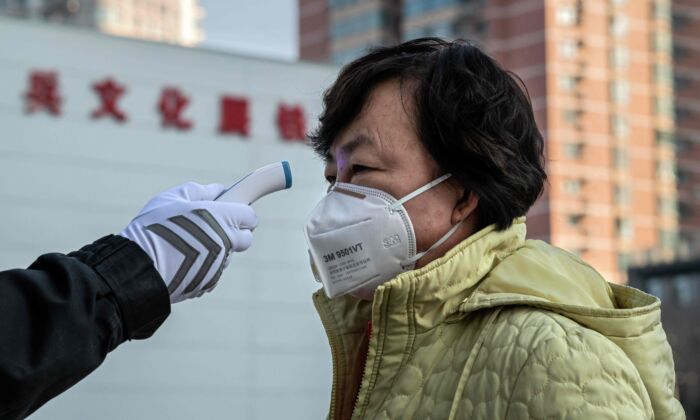 Um guarda de segurança verifica a temperatura de uma mulher usando uma máscara protetora na entrada de um parque em Pequim, China, em 31 de janeiro de 2020 (NICOLAS ASFOURI / AFP via Getty Images)