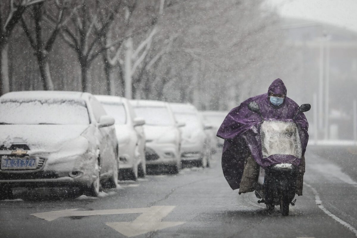 Um homem usa uma máscara protetora enquanto dirige uma motocicleta e a neve cai em Wuhan em 15 de fevereiro de 2020 (Getty Images)