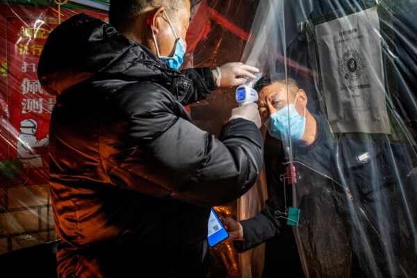 Um membro da equipe (à esquerda) verificando a temperatura corporal de um residente antes de entrar em um complexo residencial em Mudanjiang, na província de Heilongjiang, no nordeste da China, em 20 de abril de 2020 (STR / AFP via Getty Images)