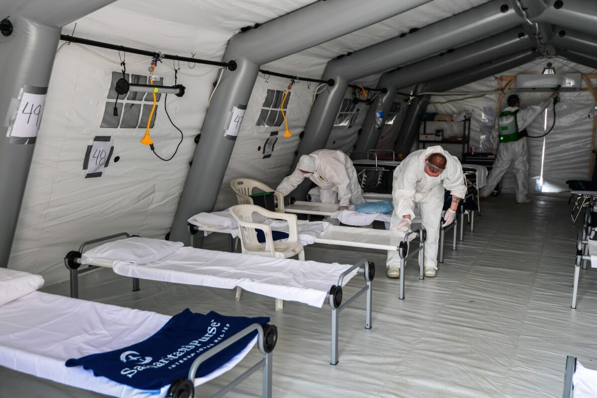 Equipe de limpeza com equipamento de proteção para desinfetar camas de pacientes em uma das lojas de um novo hospital de campanha para pacientes com coronavírus, em Cremona, sudeste de Milão, em 20 de março de 2020 (Miguel Medina / AFP / Getty Images)