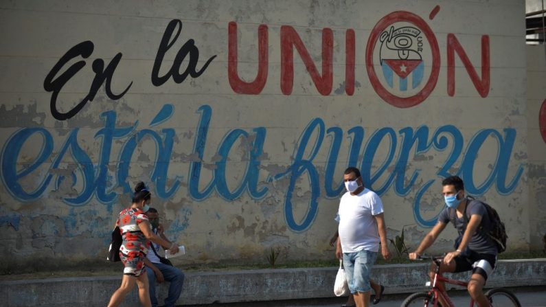 As pessoas usam máscaras perto de uma parede que lê "É na união que está a força" em uma rua de Havana, Cuba, em 13 de abril de 2020 (YAMIL LAGE / AFP via Getty Images)