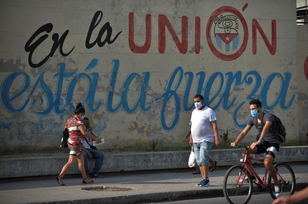 As pessoas usam máscaras perto de uma parede que lê as forças da União em uma rua de Havana, Cuba, em 13 de abril de 2020 (YAMIL LAGE / AFP via Getty Images)