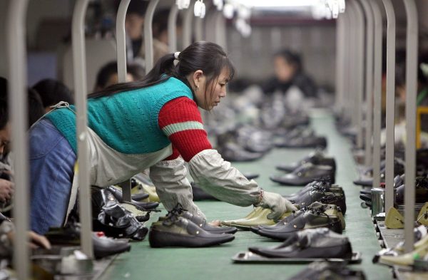 Uma funcionária tira um par de sapatos de uma linha de produção em uma fábrica localizada em Chengdu, China (Fotos da China / Getty Images)