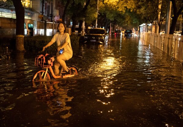 Uma mulher usa uma bicicleta para atravessar uma rua inundada após uma chuva repentina em Pequim em 9 de agosto de 2020 (NOEL CELIS / AFP via Getty Images)