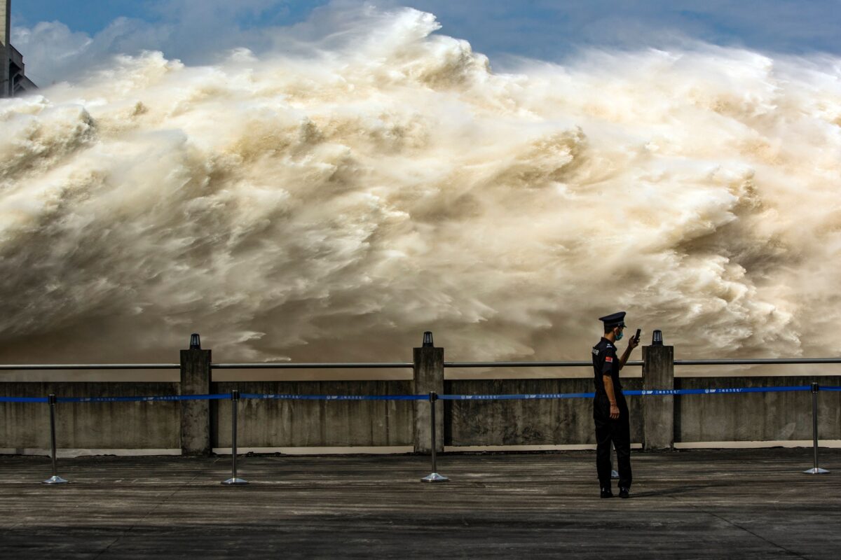 Um guarda de segurança olha para seu telefone celular enquanto a água é liberada da Barragem das Três Gargantas, um projeto hidroelétrico gigante no rio Yangtze, para aliviar a pressão das enchentes em Yichang, província de Hubei, no centro da China, em 19 Julho de 2020 (STR / AFP via Getty Images)