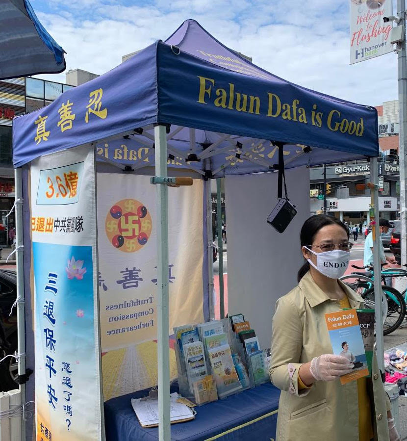 A praticante do Falun Gong Xiao Ping em frente a um estande relatando sobre a perseguição da prática espiritual na China em Flushing, Nova York, em 1º de outubro de 2020. (Cortesia do Epoch Times)