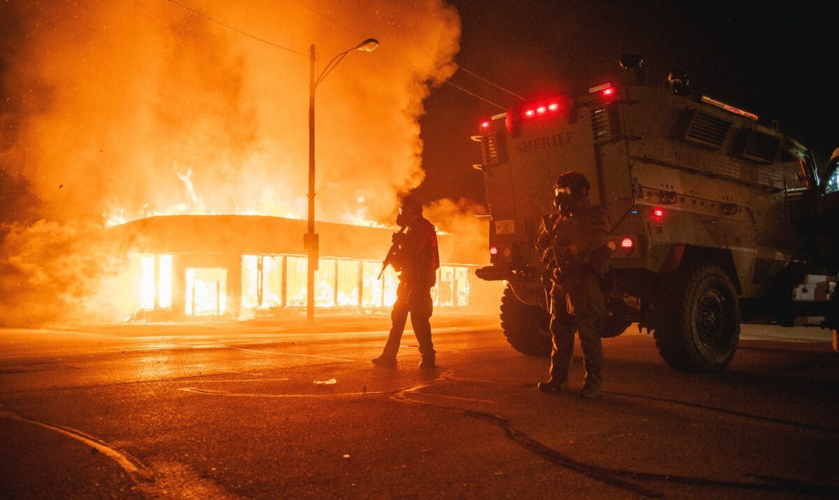 Uma viatura policial blindada em um cruzamento enquanto um prédio está pegando fogo devido aos incêndios causados ​​pelos manifestantes em Kenosha, Wisconsin, em 24 de agosto de 2020 (Brandon Bell / Getty Images)