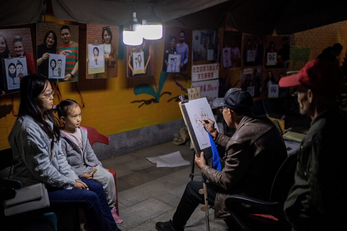 Uma mulher e uma menina posando para um retrato em um estande de artista em uma rua no distrito de artes 798 de Pequim, China, em 18 de outubro de 2020 (NICOLAS ASFOURI / AFP via Getty Images)