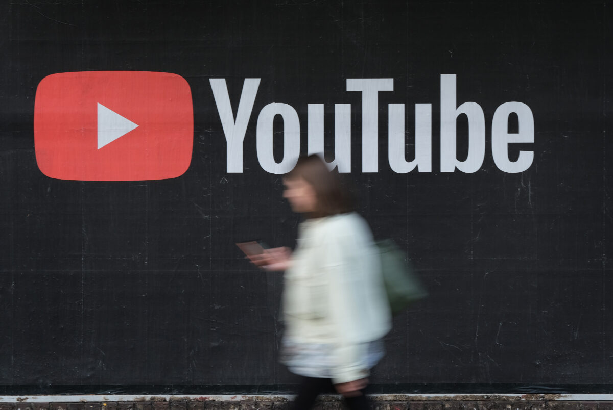 Uma mulher com um smartphone passa por um anúncio em outdoor do YouTube em Berlim em 27 de setembro de 2019 (Sean Gallup / Getty Images)