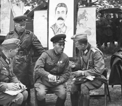 Oficiais soviéticos e alemães socializando durante uma celebração de vitória na Polônia em 22 de setembro de 1939. Um pôster de Stalin está pendurado atrás deles (Bundesarchiv, Bild/CC-BY-SA 3.0)