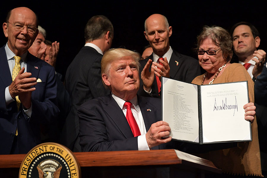 O presidente dos Estados Unidos, Donald Trump, documento assinado com novas diretrizes políticas sobre Cuba, ao fundo a dissidente cubana, Cary Roque (Mandel Ngan / AFP / Getty Images)