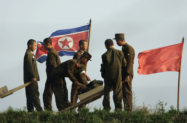 Soldados norte-coreanos trabalham em terras agrícolas perto da bandeira nacional nos arredores da cidade de Sinuiju em 18 de outubro de 2006. (Cancan Chu/Getty Images)