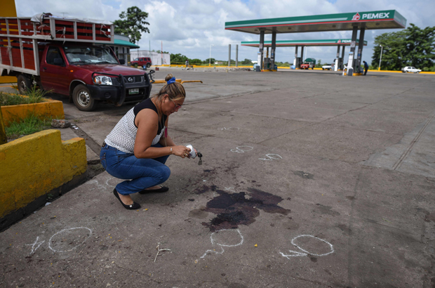 Um parente coloca uma vela ao lado das marcas de sangue que permanecem no local onde o jornalista mexicano Candido Rios foi morto, em frente a um posto de gasolina em Hueyapan de Ocampo, no estado de Veracruz, México, em 23 de agosto de 2017 (Victoria Razo/AFP/Getty Images)