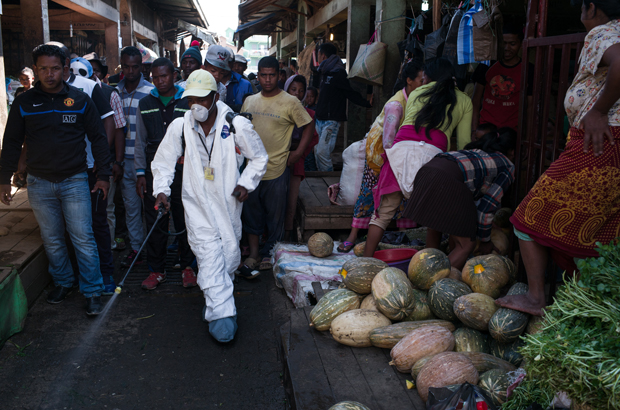 Pessoas abrem caminho enquanto um funcionário de saúde pulveriza desinfetante durante a limpeza do mercado de Anosibe, no distrito de Anosibe, um dos distritos mais insalubres de Antananarivo, Madagascar, em 10 de outubro de 2017 (Rijasolo/AFP/Getty Images)