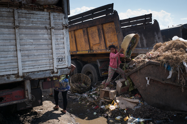 Uma menina esvazia uma cesta de lixo enquanto funcionários de saúde recolhem o lixo durante a limpeza do mercado de Anosibe, no distrito de Anosibe, um dos distritos mais insalubres de Antananarivo, Madagascar, em 10 de outubro de 2017 (Rijasolo/AFP/Getty Images)