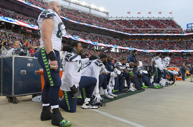 Vários jogadores do time Seahawks de Seattle permanecem sentados no banco ou se ajoelham durante o hino nacional dos EUA antes do início de um jogo da NFL contra os 49ers de São Francisco no Estádio Levi's, em Santa Clara, Califórnia, em 26 de novembro de 2017 (Thearon W. Henderson/Getty Images)