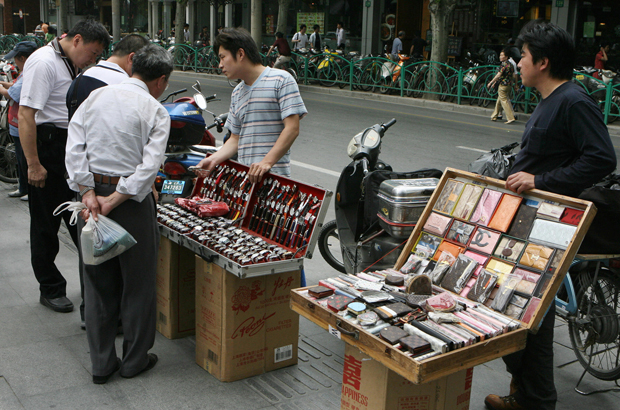 China, contrafação, falsificação - O funcionário lustra uma bolsa falsa Prada enquanto sentado entre outros produtos falsificados na cidade de Cantão, China, em 18 de novembro de 2004 (Laurent Fievet/AFP/Getty Images)